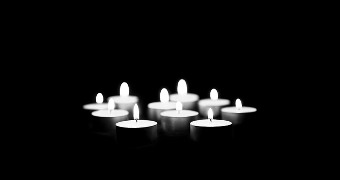 Black and white photo of ten memorial tealights lit and grouped together against a black background
